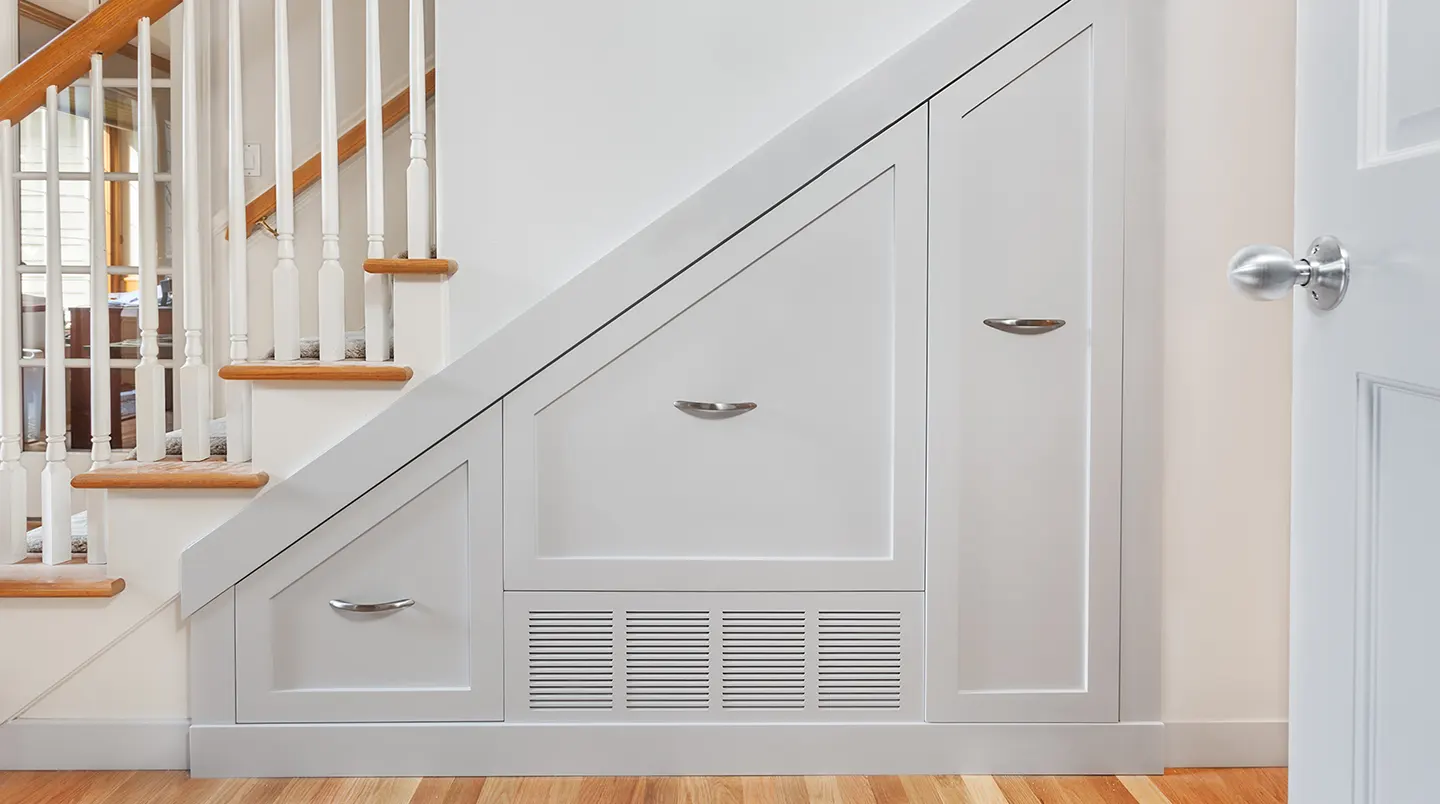 Placard sur mesure aménagé sous un escalier intérieur français, portes ouvertes révélant étagères ajustées à la pente, tiroirs bas et penderie en hauteur avec rangement organisé